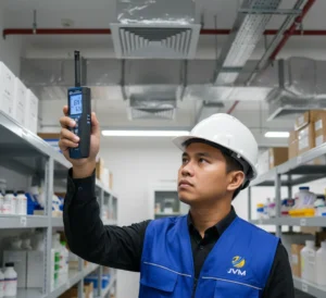 Teknisi Indonesia menggunakan climate meter PCE-330-ICA untuk mengukur suhu dan kelembapan di ruang penyimpanan laboratorium dengan latar rak dan sistem HVAC.