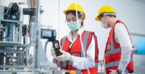 Seorang teknisi Indonesia menggunakan sound level meter portabel di area industri untuk mengukur tingkat kebisingan mesin produksi secara langsung.